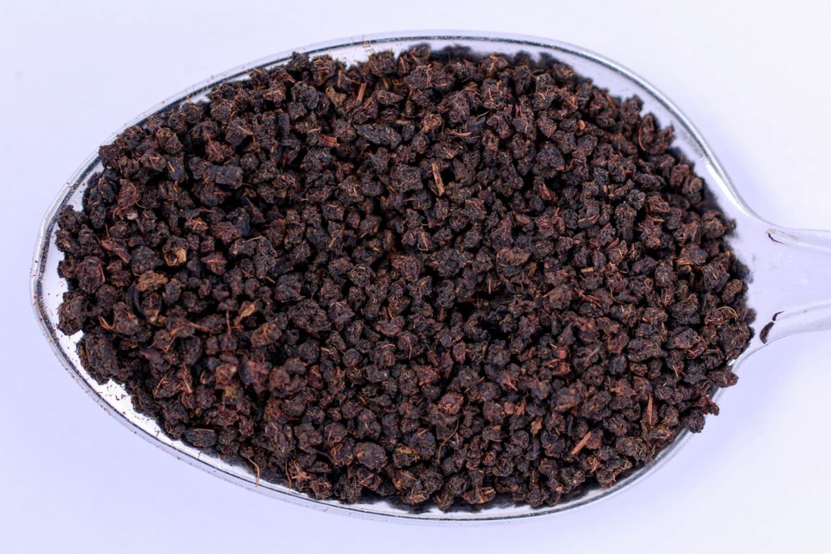 Loose black tea granules heaped on a spoon