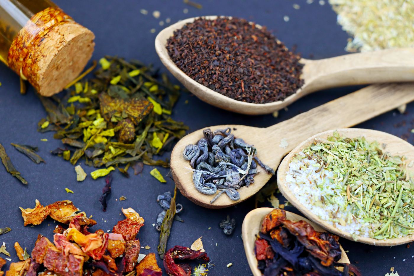 Several distinct loose leaf tea blends, from black to herbal, laid out on wooden spoons
