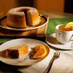 Slice of cake on a plate beside a cup of tea garnished with orange