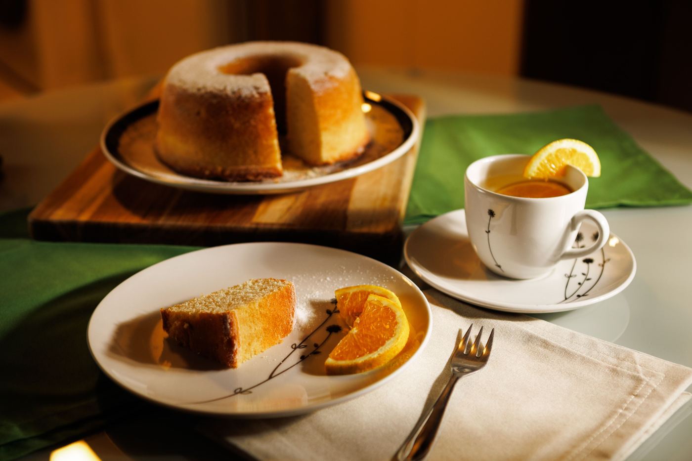 Slice of cake on a plate beside a cup of tea garnished with orange