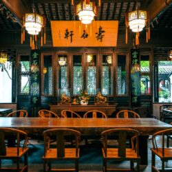 A traditional Chinese tea house interior with hanging lanterns, carved wood screens, and a long communal table
