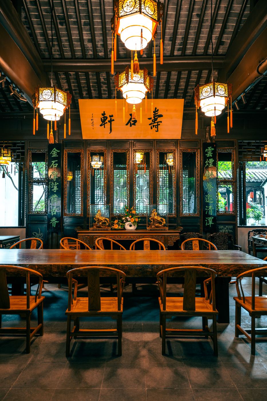 A traditional Chinese tea house interior with hanging lanterns, carved wood screens, and a long communal table