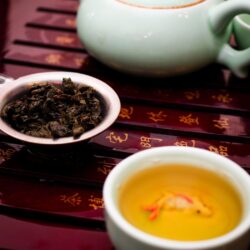 Rolled Tie Guan Yin oolong tea leaves in a gaiwan lid beside a cup of golden brewed tea