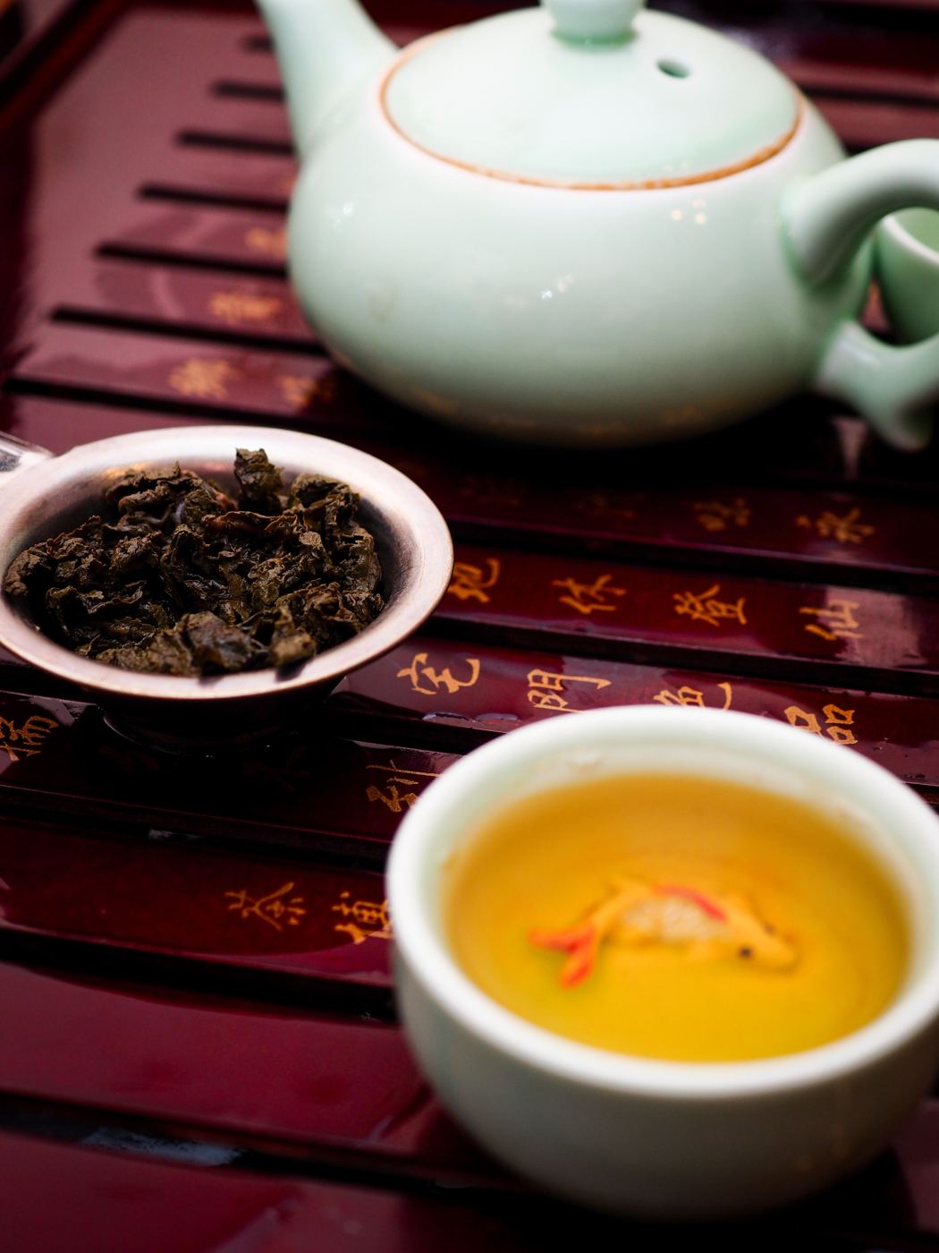 Rolled Tie Guan Yin oolong tea leaves in a gaiwan lid beside a cup of golden brewed tea