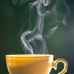 Steaming pale golden tea in a yellow ceramic cup against a dark background