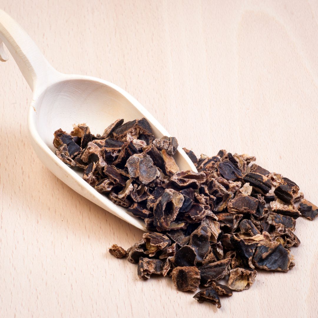 Wooden scoop filled with roasted carob chips on a light wooden background, highlighting their nutty sweetness and antioxidant-rich properties.