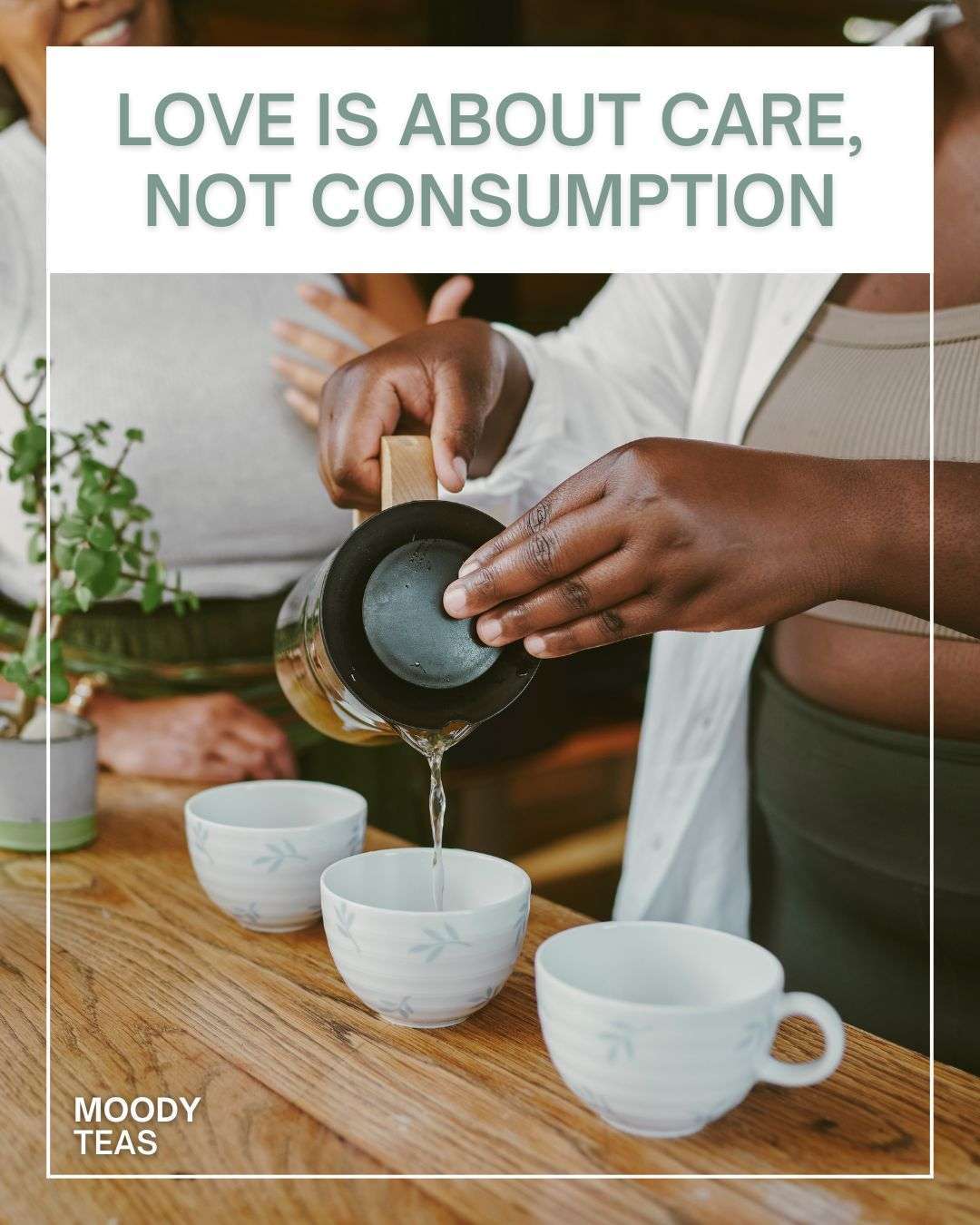 A person pours hot tea from a glass teapot into small white ceramic cups on a wooden table, with another person sitting nearby. The scene shows a shared tea moment in a warm, natural setting. Text over the image reads “Love is about care, not consumption,” with Moody Teas branding in the corner.